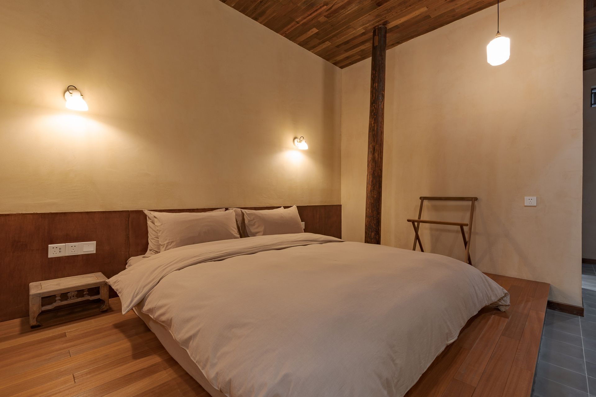 Cozy rustic bedroom with a large bed, warm wall lights, and wood-beam ceiling