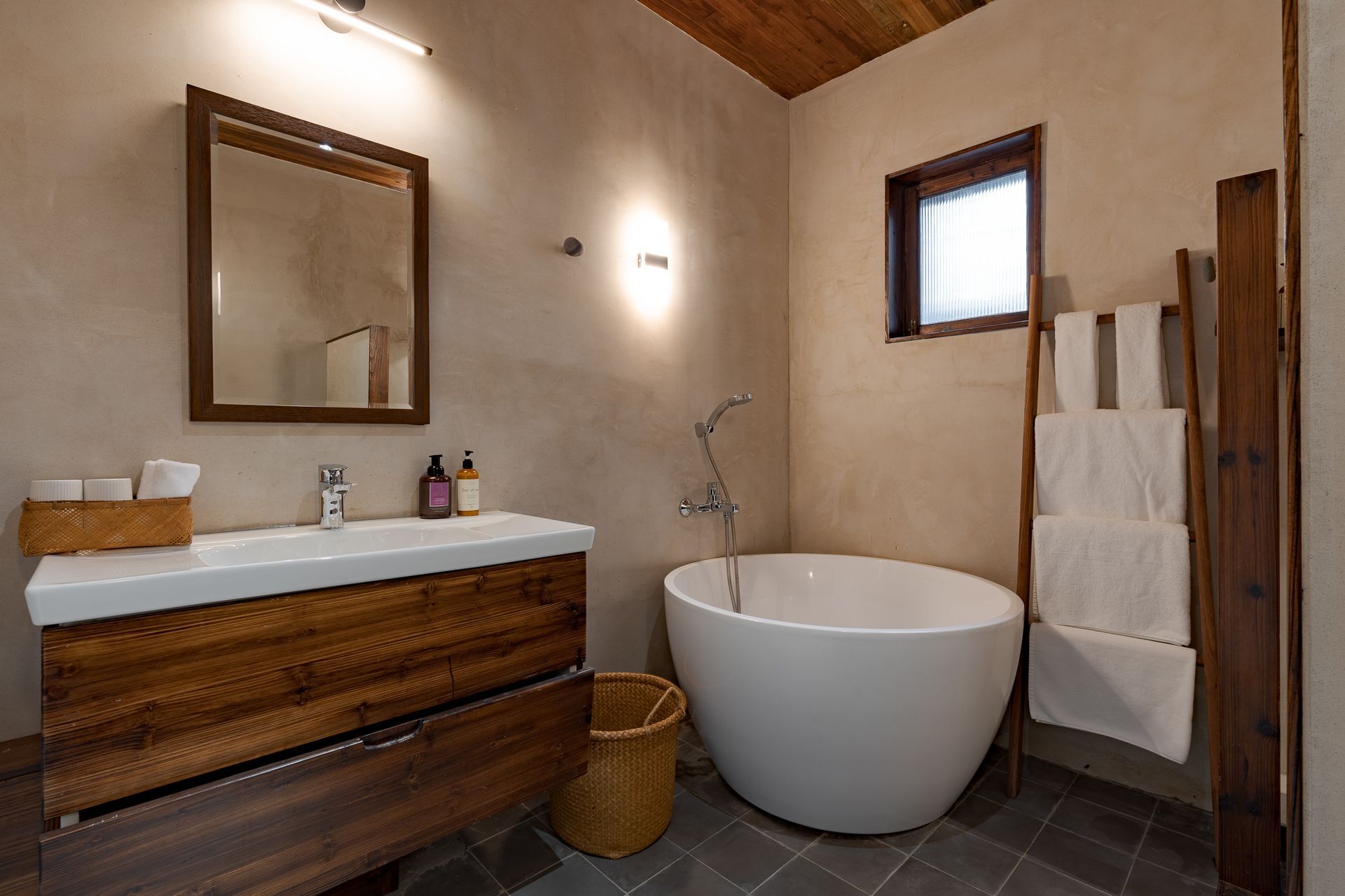 Modern bathroom with wood vanity, round tub, mirror, and towel rack on beige walls