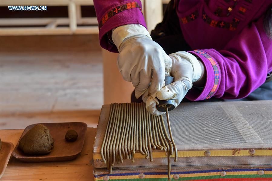 Hands in white gloves weaving a colorful textile on a loom.
