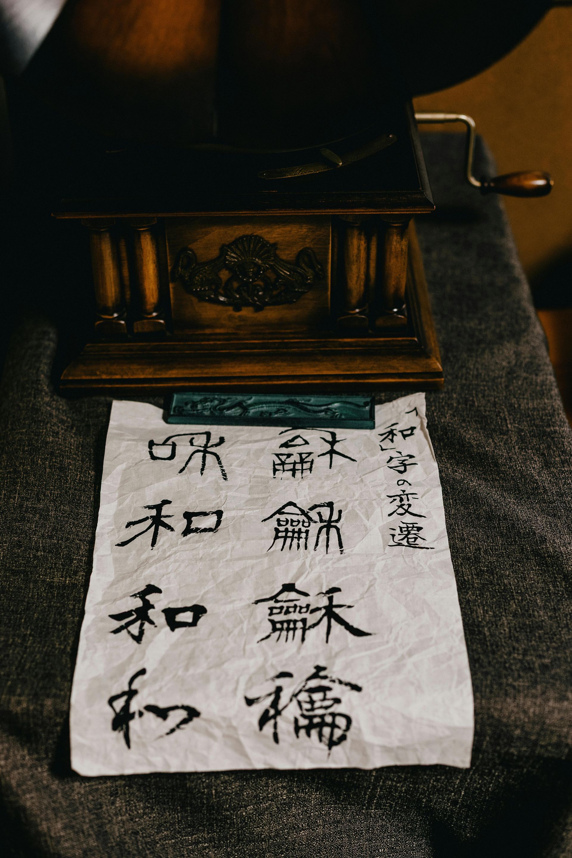 White paper with black Japanese calligraphy hanging beneath a dark wooden shrine or altar.
