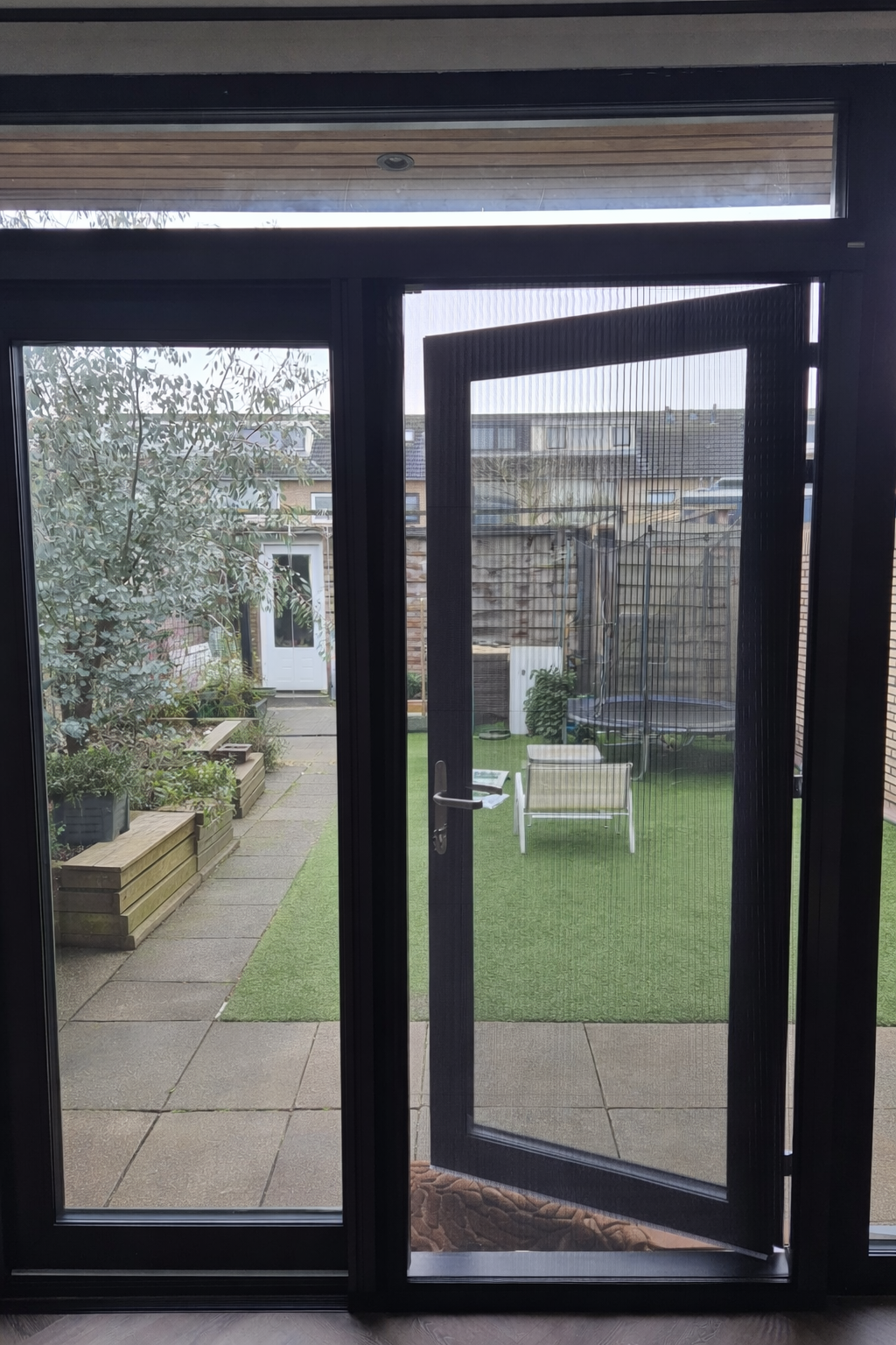 Open glazen deur naar een terras met kunstgras, tuinmeubilair en daarachter een schuur.