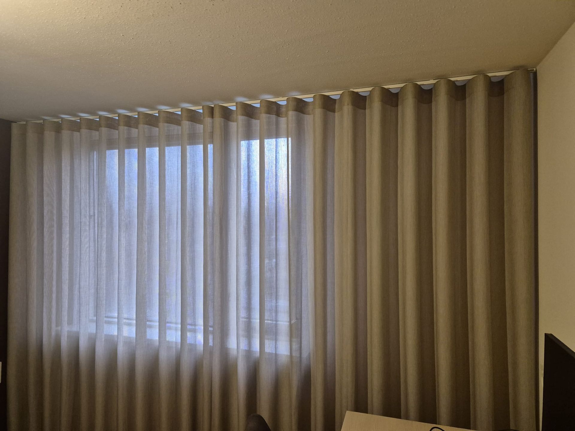 Dunne gordijnen voor een zonnig raam in een beige kamer.