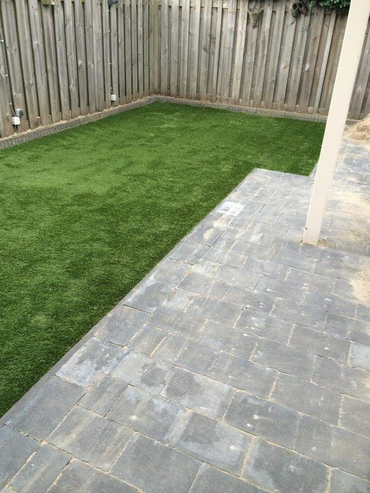 Terras in de achtertuin met grijze bestrating naast een groen gazon en een houten schutting.