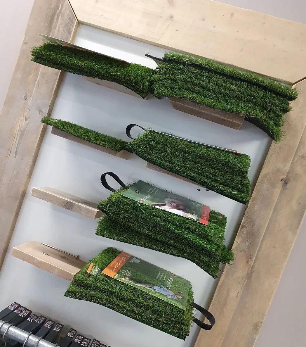 Groene kunstgrasmatten opgestapeld op houten planken in een winkelpresentatie.