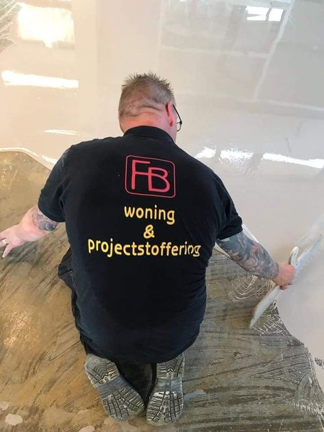 Een medewerker in een zwart FB-shirt knielt op een gepolijste vloer tijdens installatiewerkzaamheden.