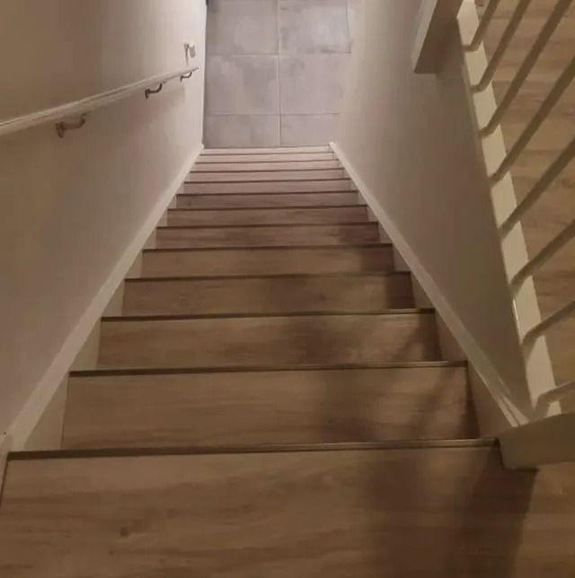 Houten trap, van onderaf gezien, met witte muren, een leuning aan de linkerkant en een balustrade aan de rechterkant.