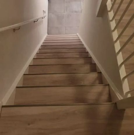 Houten trap, van onderaf gezien, met witte muren, een leuning aan de linkerkant en een balustrade aan de rechterkant.