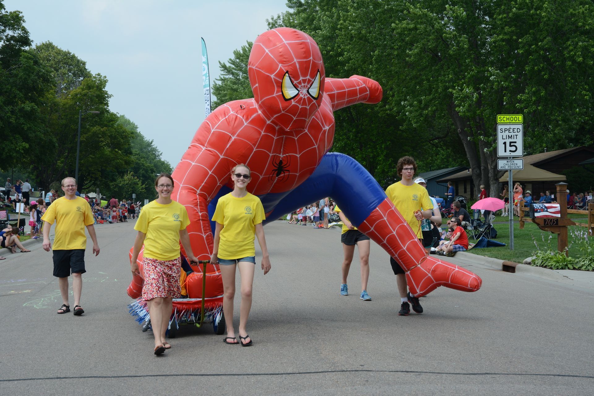 People walking beside a giant red Spider-Man inflatable on a park path.