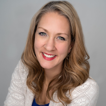 Smiling woman with wavy blonde hair in a white top against a gray background