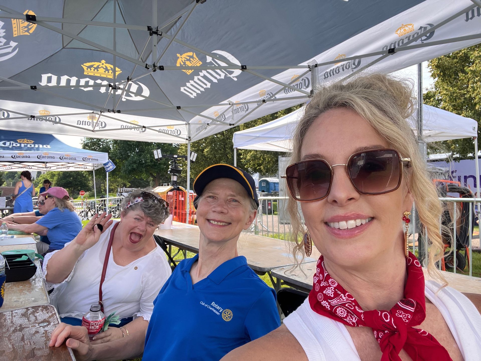 Three people posing under a branded canopy at an outdoor event, smiling with drinks in hand.