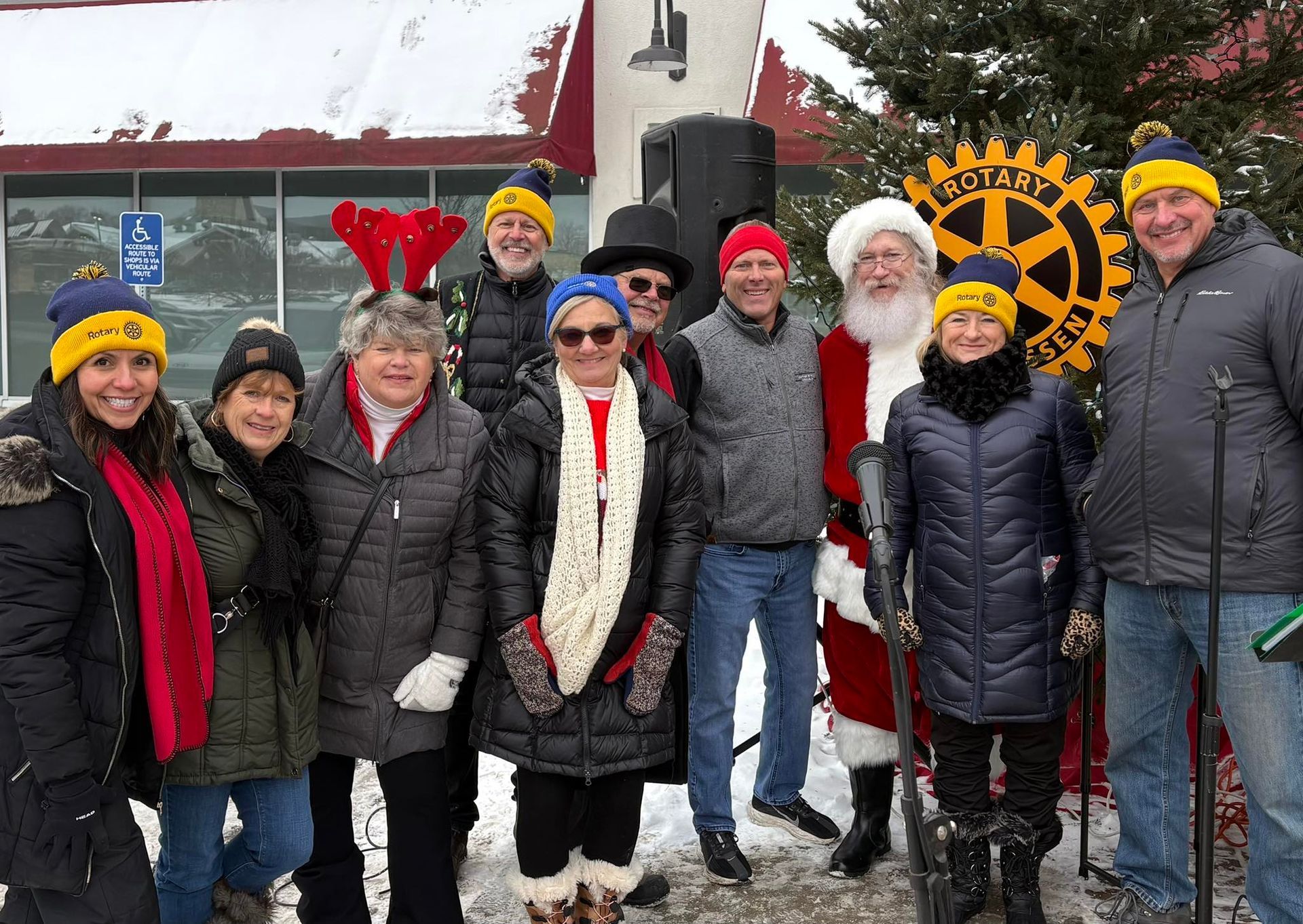Group of people in winter clothes posing in the snow beside a building and a large yellow gear sign