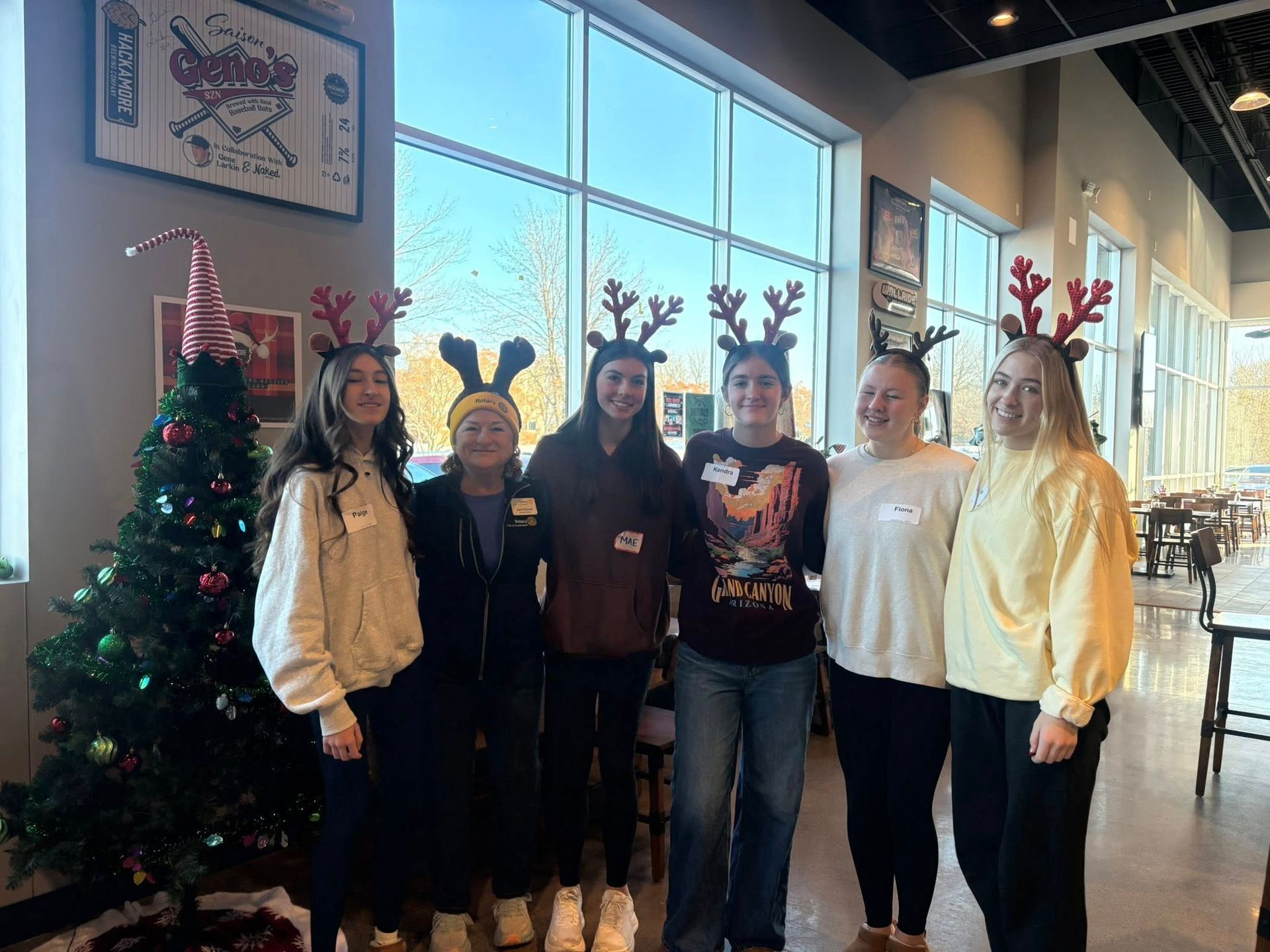 Group in holiday reindeer antlers posing beside a decorated Christmas tree in a bright indoor lobby