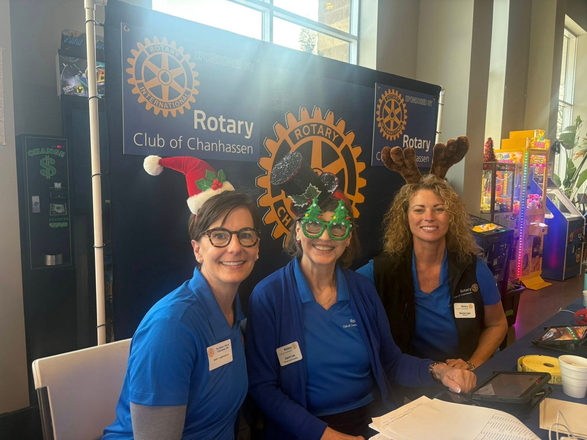 Three Rotary Club volunteers in blue shirts smile at a booth with Rotary Club banners.