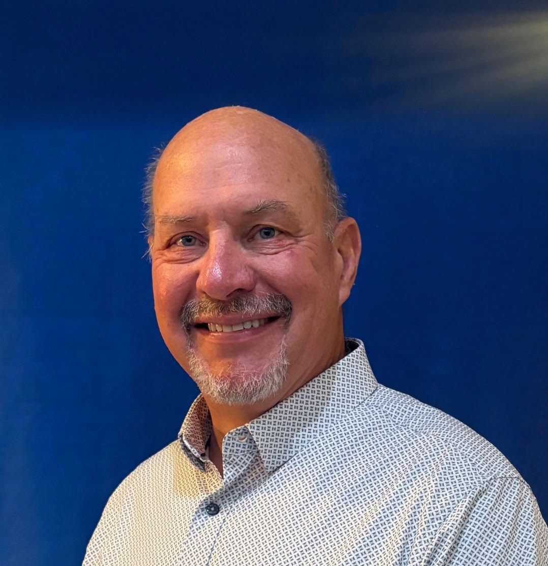 Smiling man in a patterned shirt against a blue background