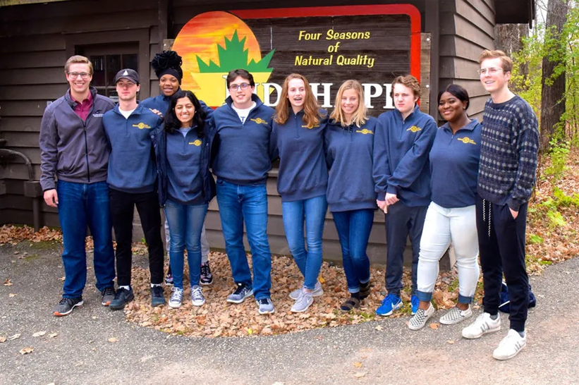 Group of people in blue jackets standing outside a sign for a forest school organization