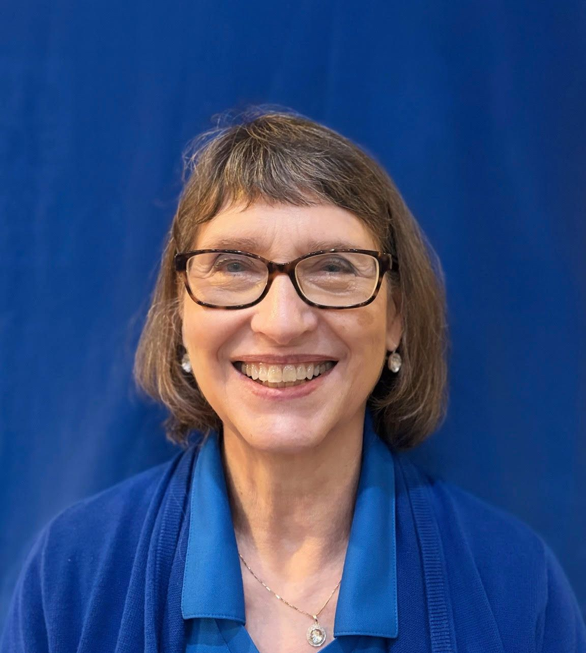 Smiling person with glasses and short brown hair in blue clothing against a blue background