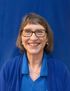 Smiling woman in glasses wearing a blue top against a blue backdrop