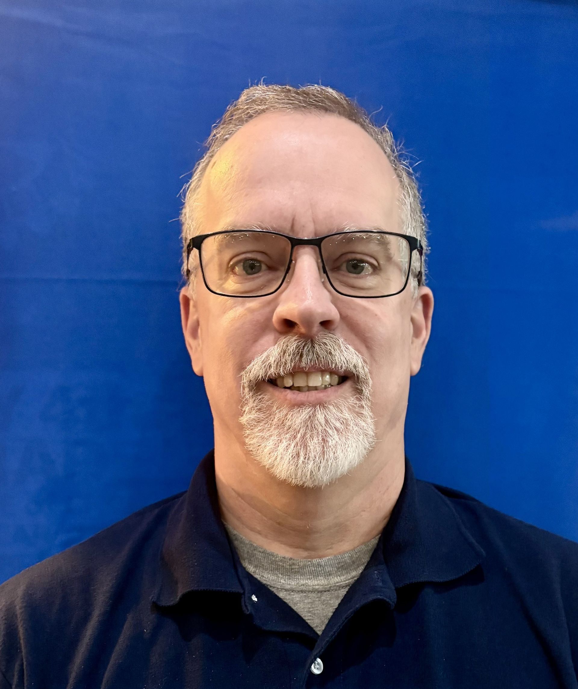 Portrait of a man in glasses and a navy shirt against a bright blue background