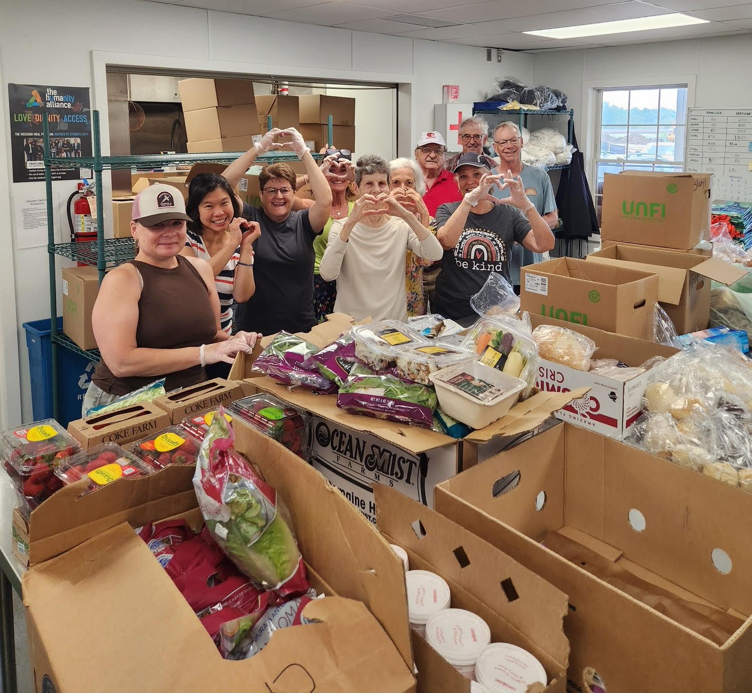 Volunteers packing food boxes in a donation room, with supplies piled on tables and shelves.