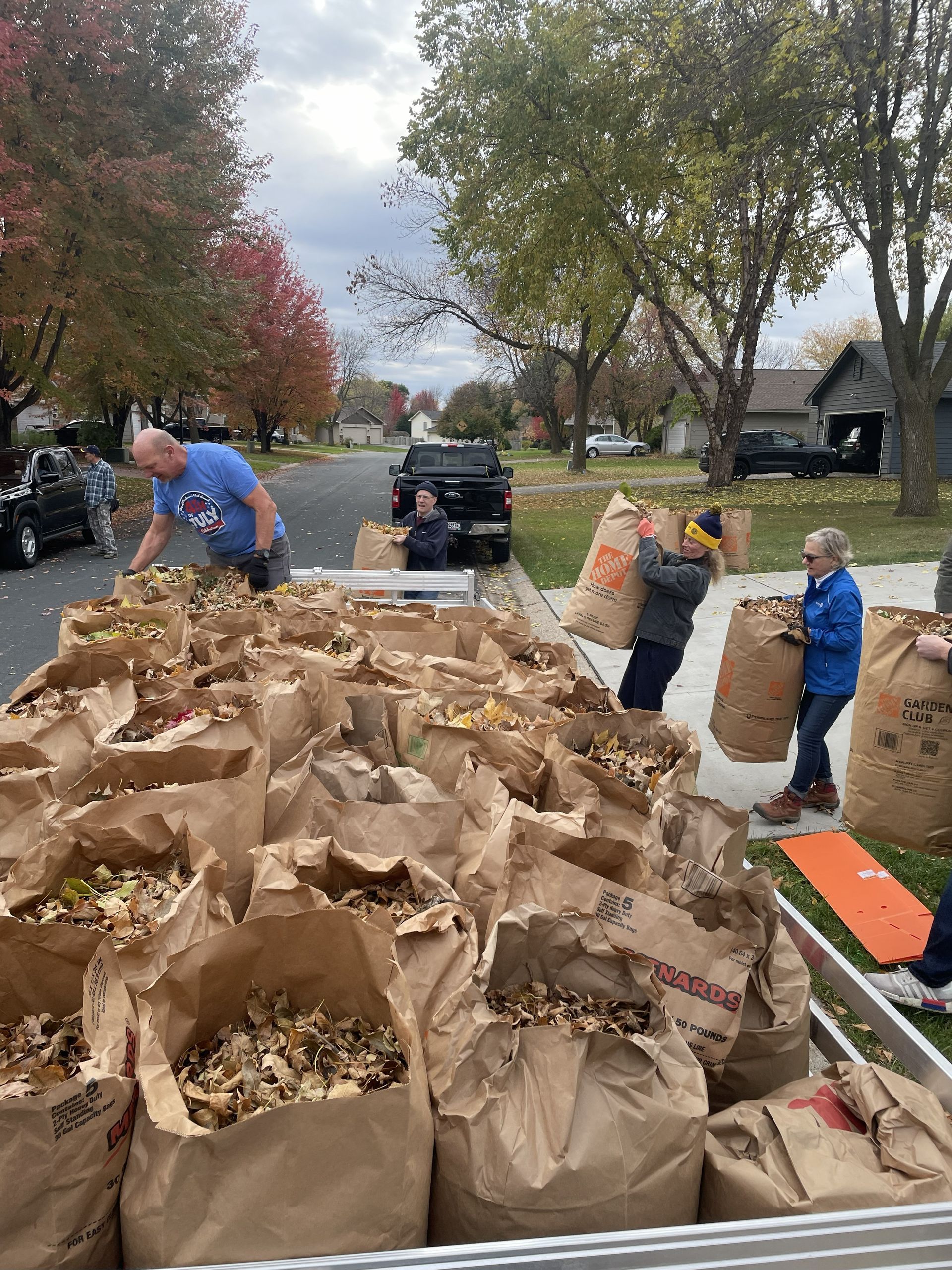 People loading leaf-filled bags onto a truck on a tree-lined street in autumn.