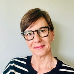 Portrait of a person with short brown hair and black glasses, wearing a navy-and-white striped top, smiling gently.