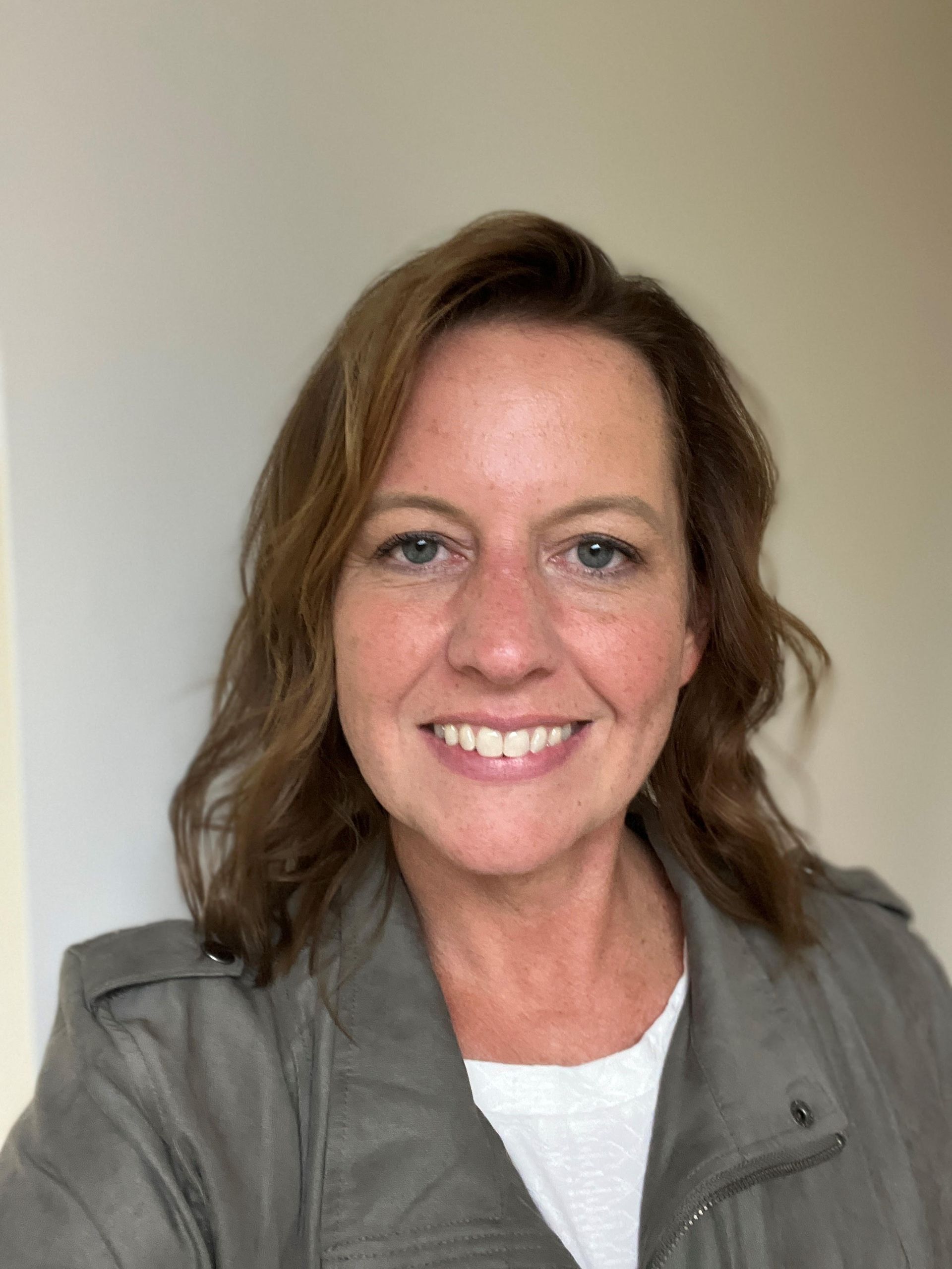 Smiling person in a gray jacket against a plain light background