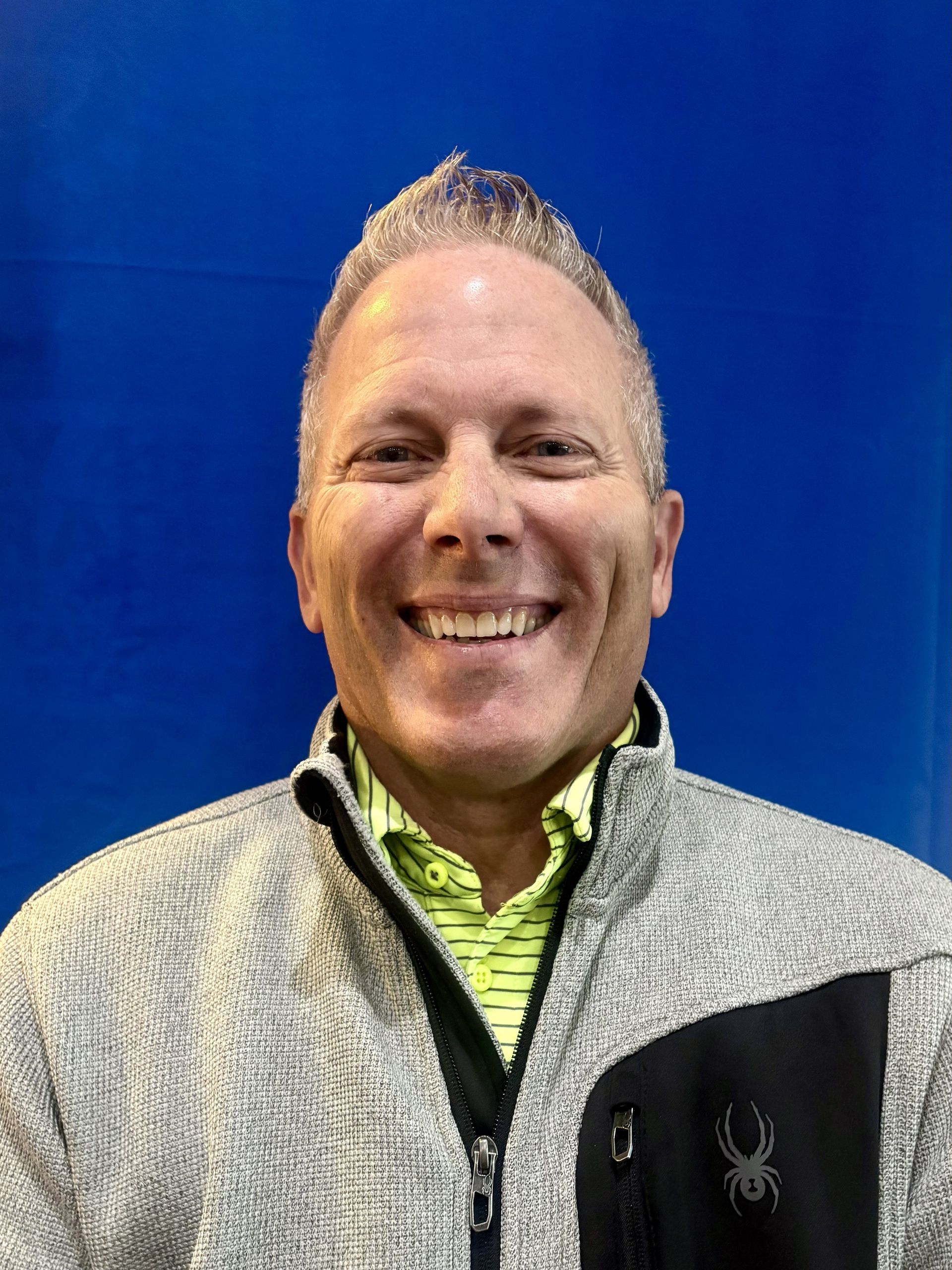 Smiling person in a gray jacket against a blue background