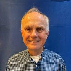 Smiling person in a gray jacket against a blue background