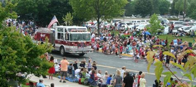 Crowd watches a red-and-white parade truck driving down a wet street lined with spectators.