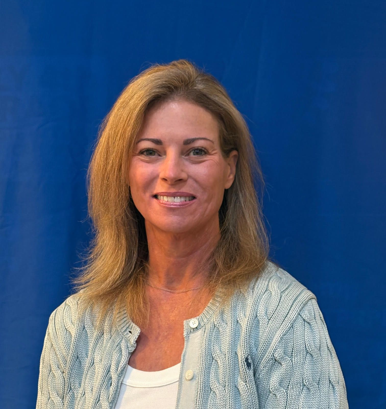 Woman smiling against a blue backdrop, wearing a light blue cardigan over a white top