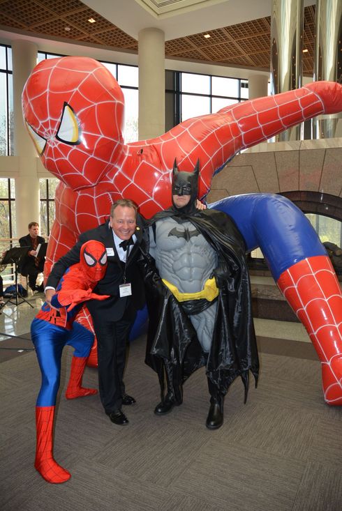 Spider-Man, Batman, and two people posing beside a giant Spider-Man statue in a lobby