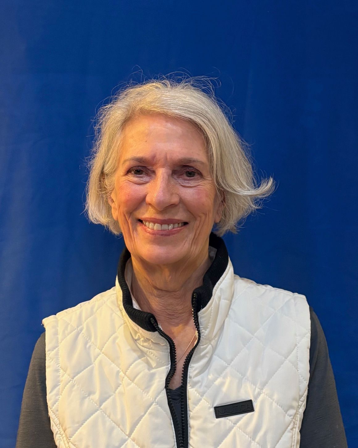 Smiling person in a white quilted vest standing before a blue background.