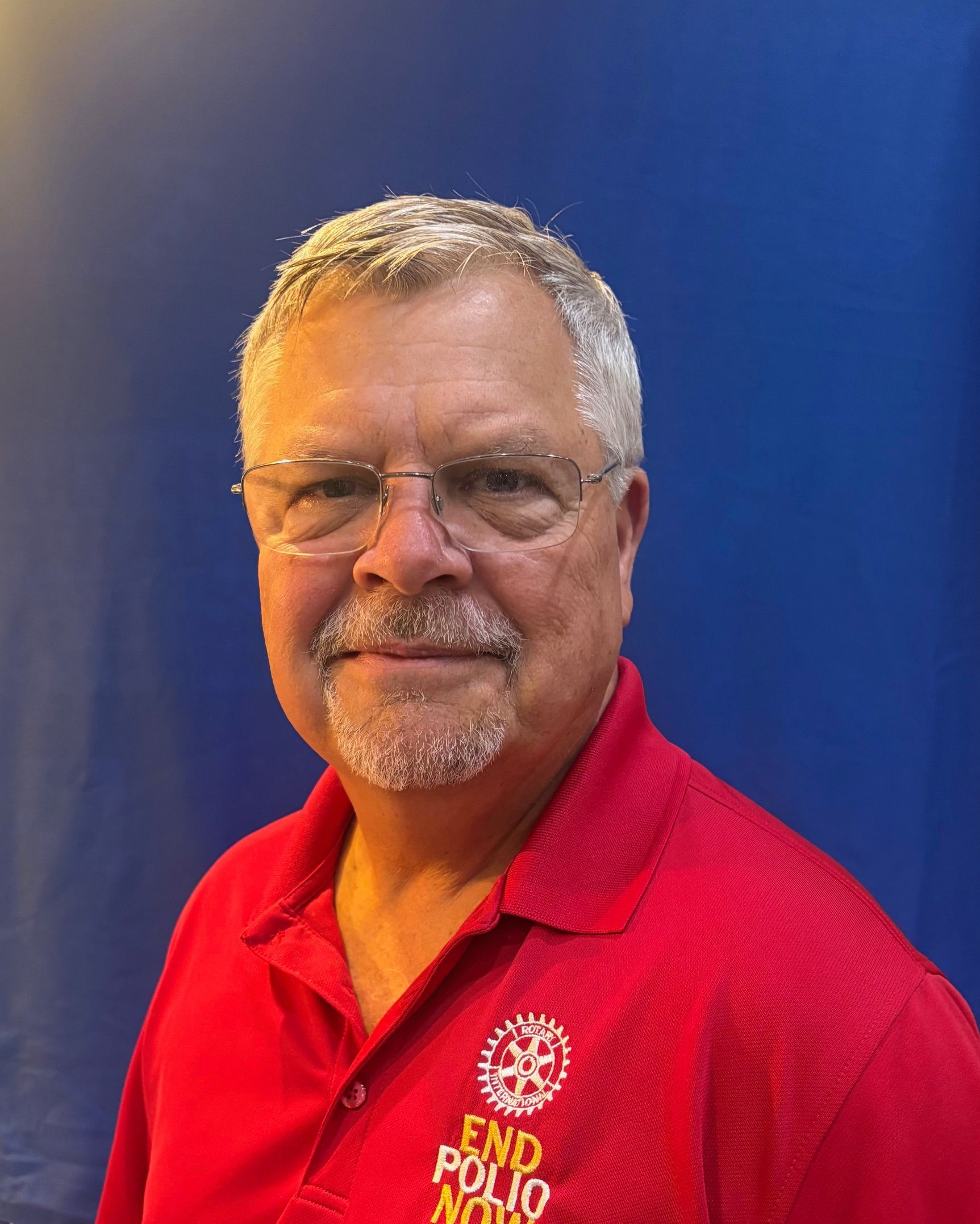 Smiling man in glasses wearing a red polo shirt against a blue background
