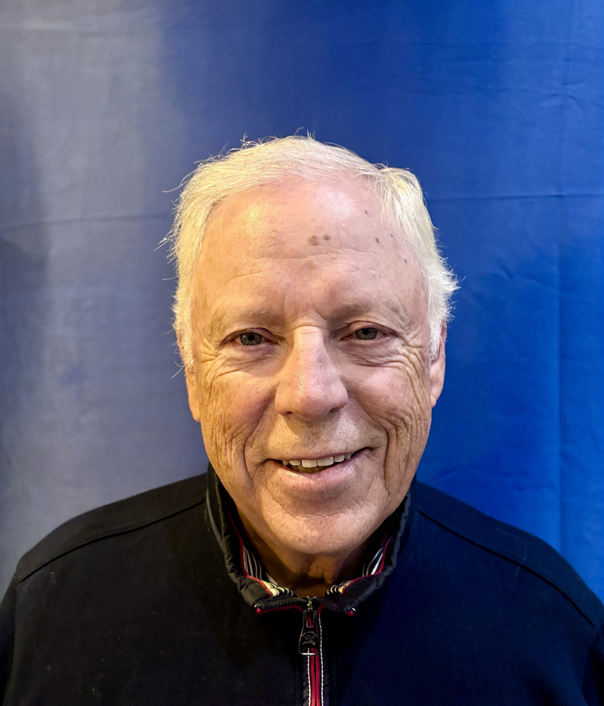 Smiling person in a black jacket against a blue background