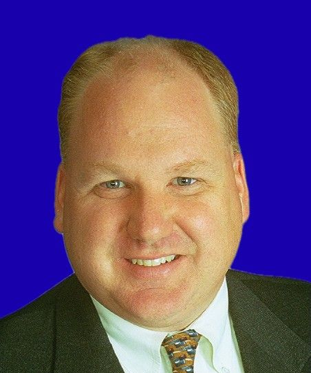 Smiling man in a dark suit and patterned tie against a blue background