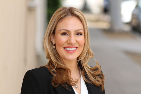 A woman is sitting at a desk with a laptop and a vase of flowers.