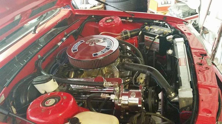The engine of a red car is shown with the hood open.