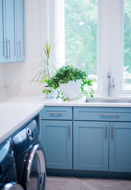 A laundry room with blue cabinets , a washer and dryer , a sink , and a window.