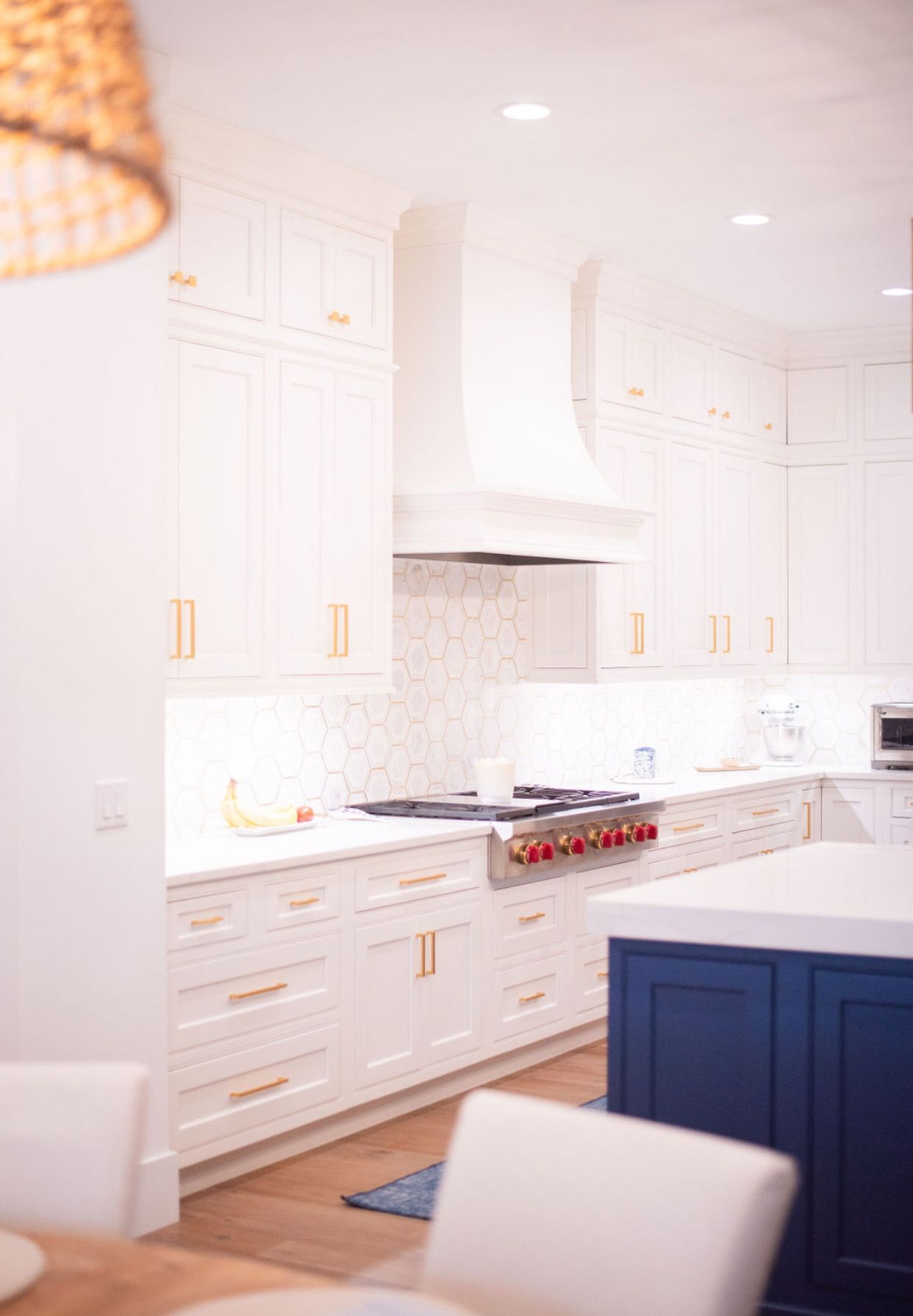 Bright white modern kitchen with navy island, marble counters, brass accents, and built-in range hood