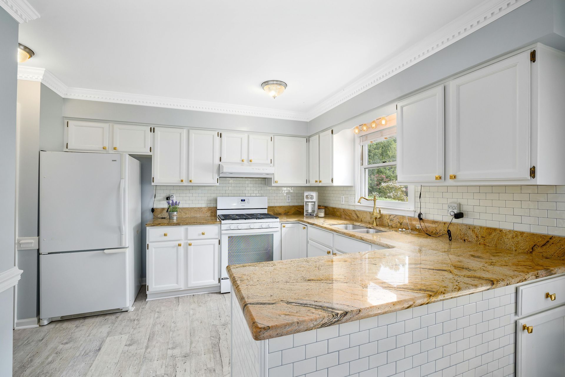 Bright white kitchen with granite counters, white cabinets, stainless appliances, and a tiled floor