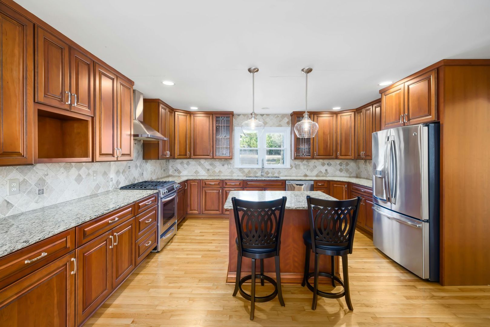 Bright kitchen with wooden cabinets, stainless fridge, and a central island with two chairs.