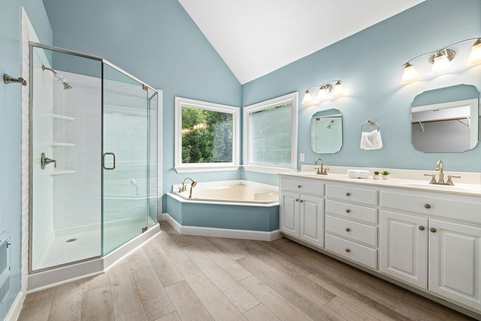 Bright blue bathroom with glass shower, corner tub, and double vanity under skylights
