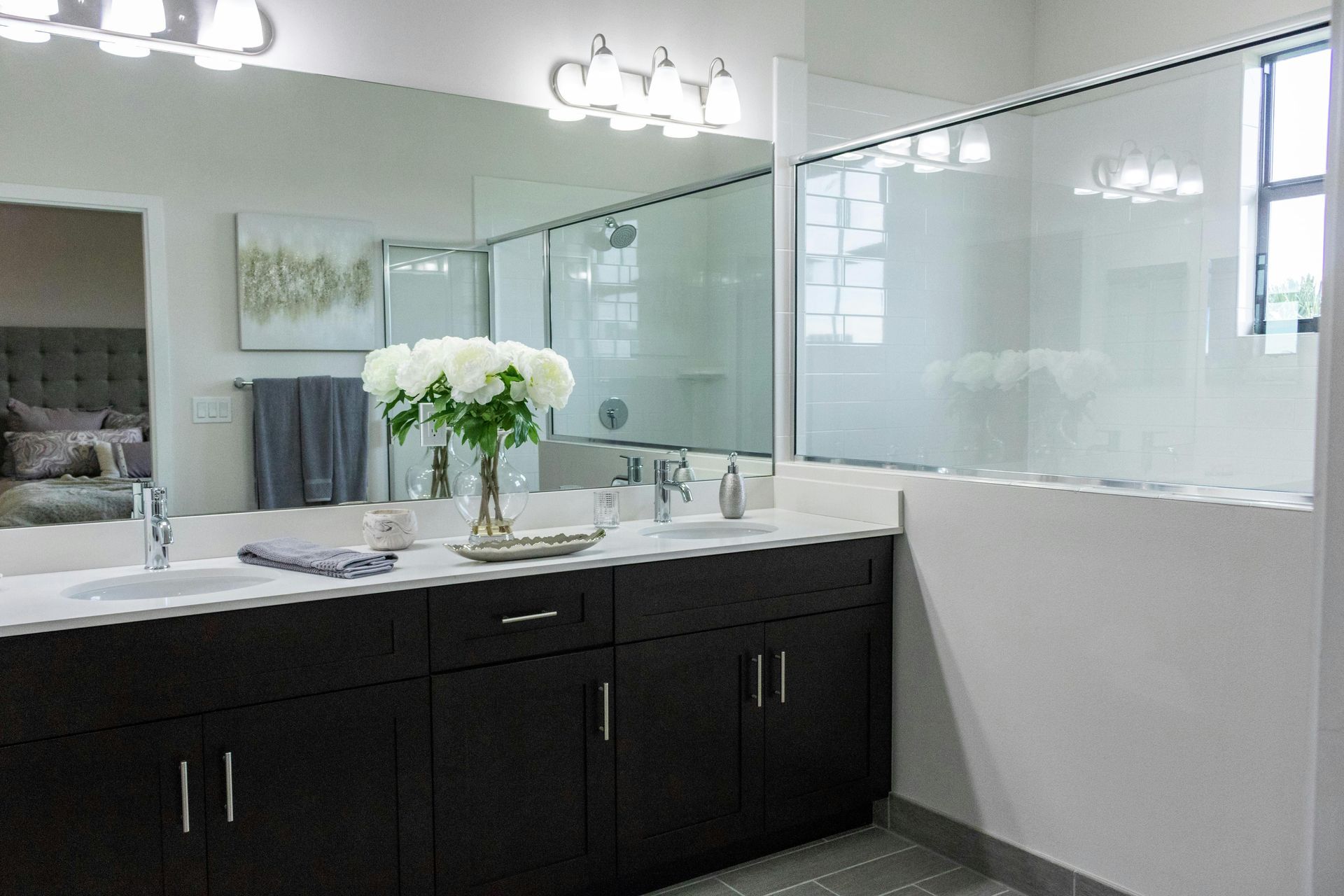 Modern bathroom vanity with dark cabinets, white countertop, mirror, and frosted glass shower enclosure