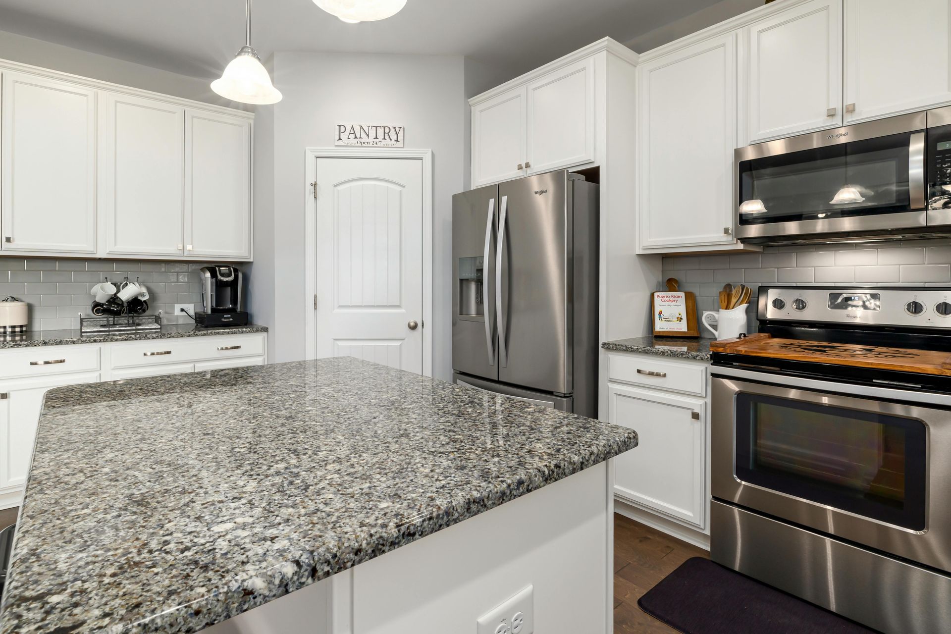 Bright modern kitchen with white cabinets, granite island, and stainless steel appliances