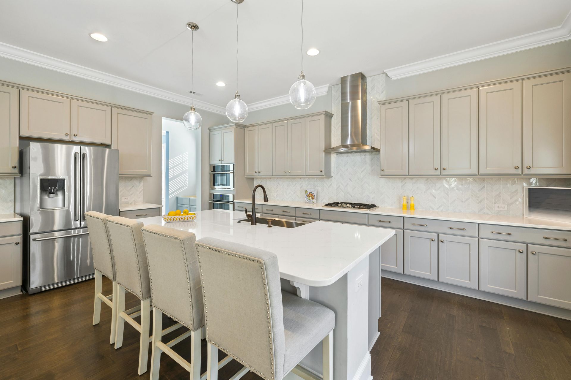 Bright modern kitchen with white island, beige cabinets, stainless steel appliances, and pendant lights
