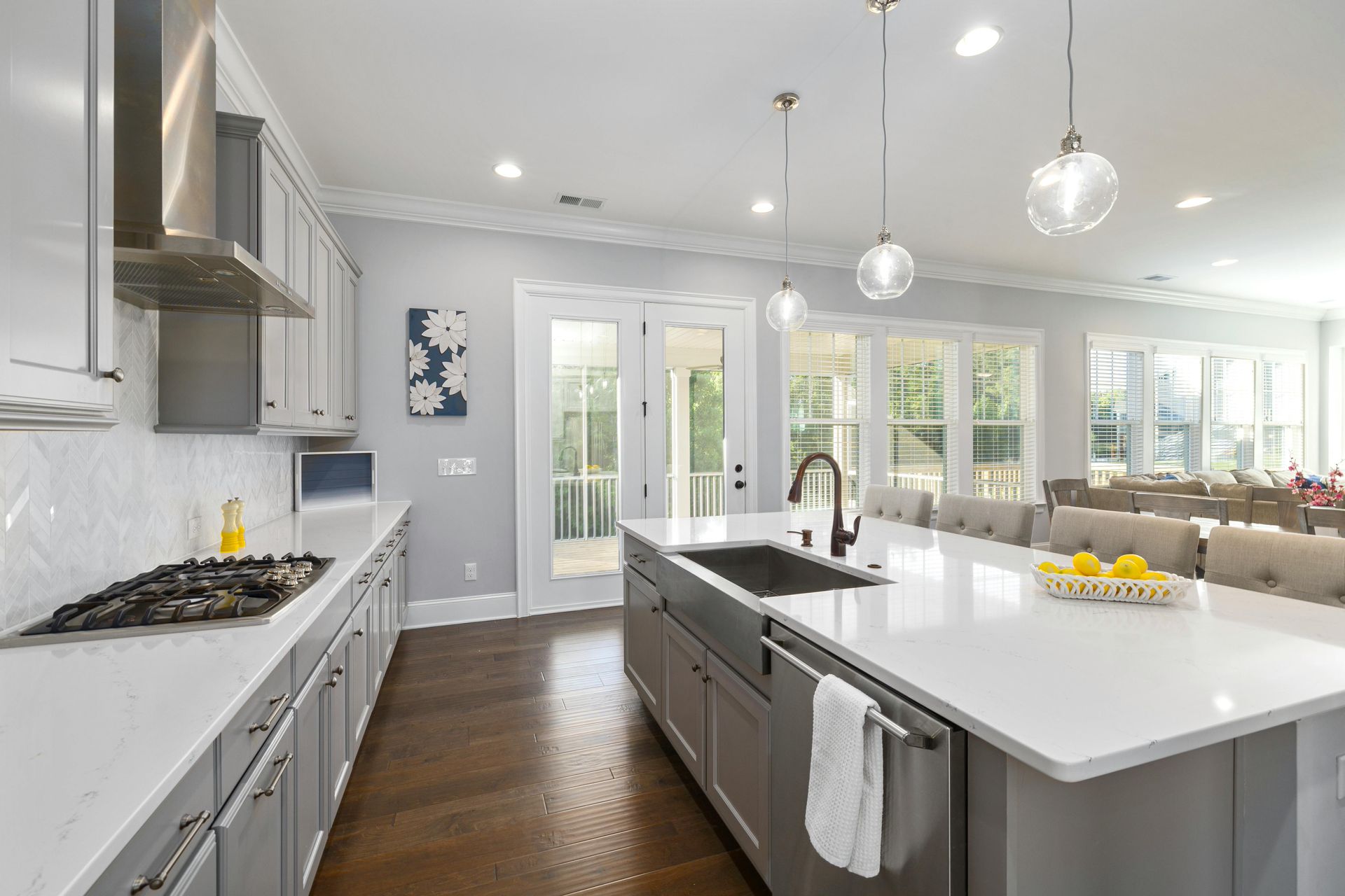 Bright modern kitchen with white cabinets, gray island, hardwood floors, and pendant lights