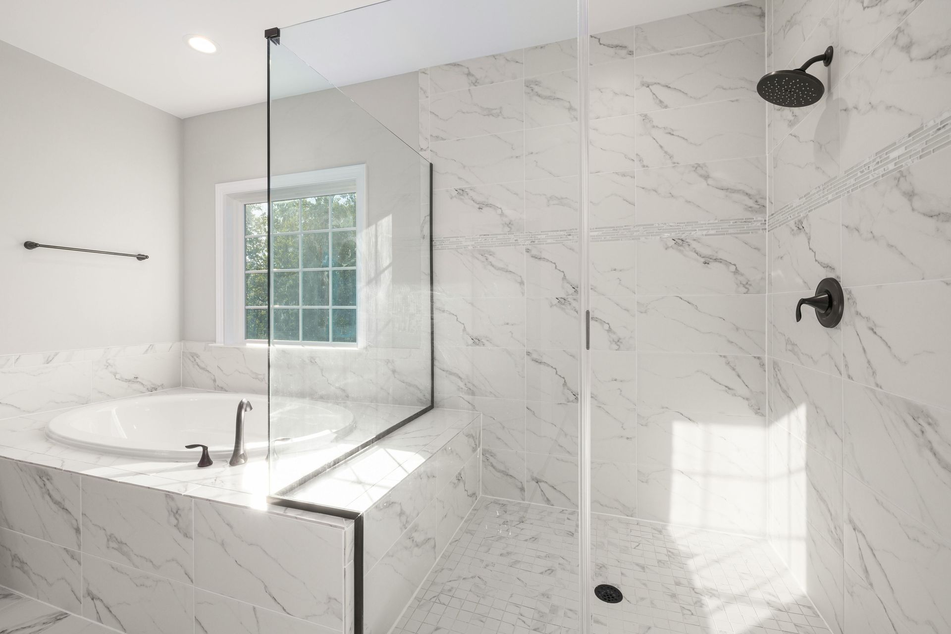 Bright marble bathroom with glass shower, freestanding tub, and window light