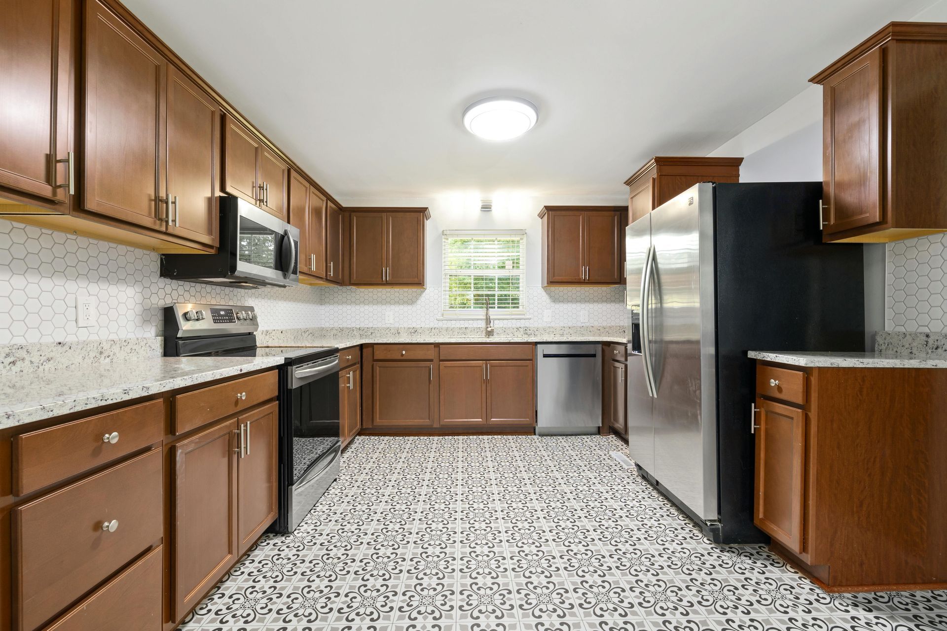 Modern kitchen with wood cabinets, speckled countertops, stainless fridge, and tiled floor.