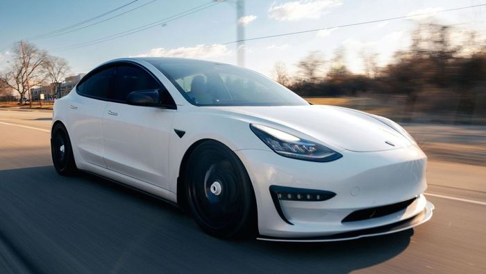 A white tesla model 3 is driving down a road.
