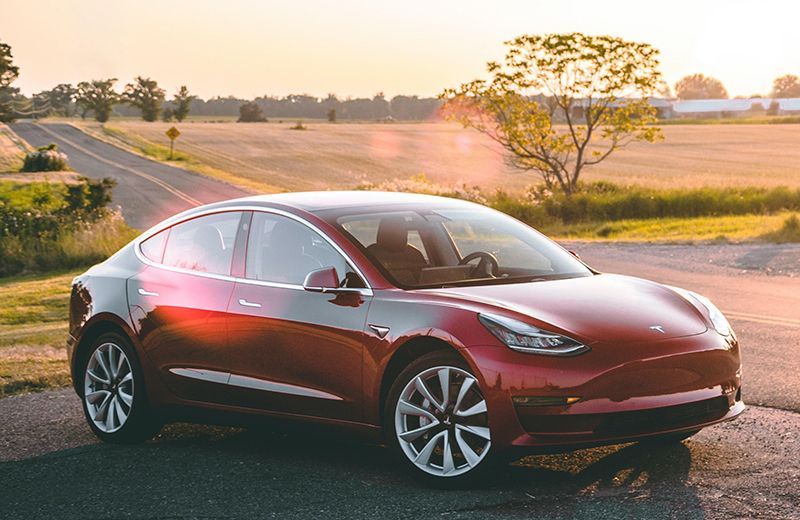A red tesla model 3 is parked on the side of the road.